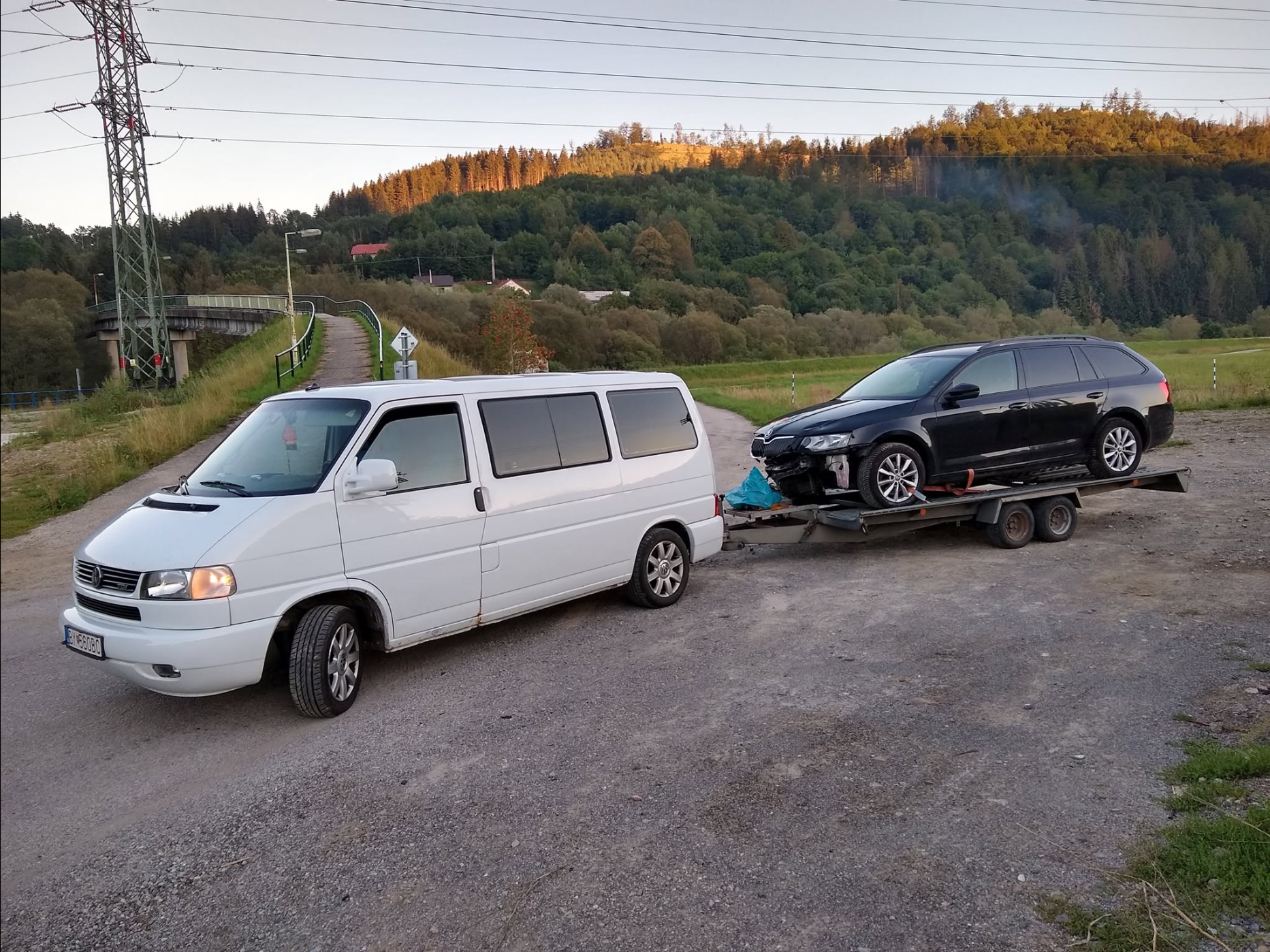 Biela dodávka VW s prívesom odváža poškodenú Škodu Octavia, v pozadí kysucké kopce pri západe slnka