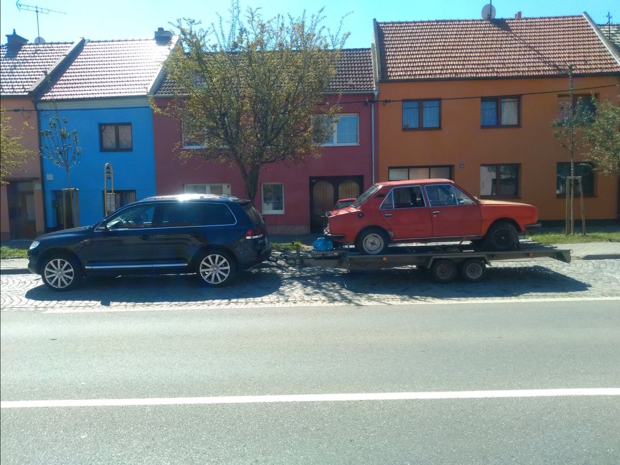 Červená Škoda 105 na prívese pred farebnými domami