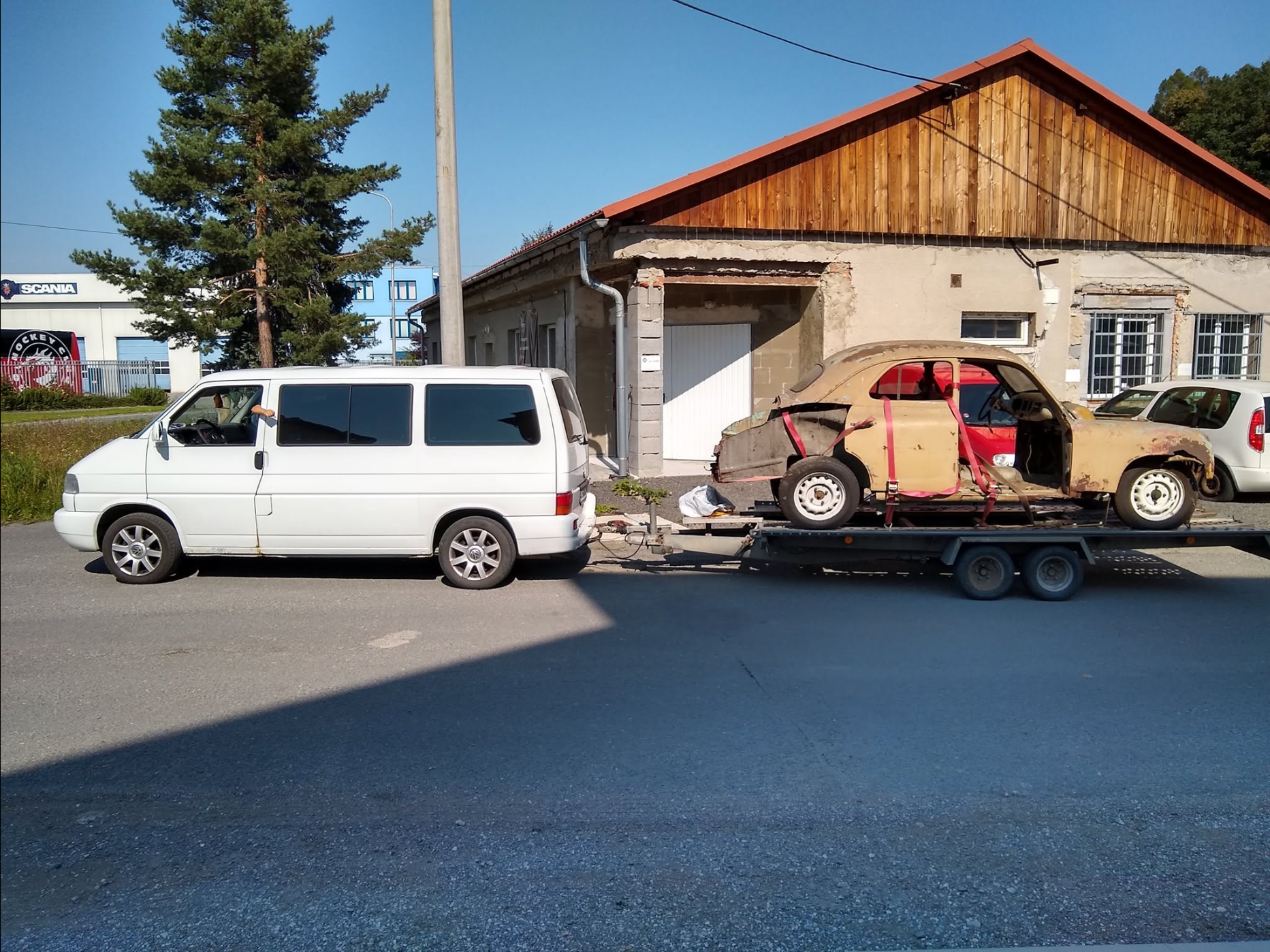 Karoséria historickej Škody 1101 Tudor pripútaná na prívese za bielou dodávkou VW